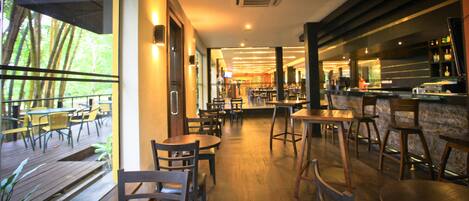 Un comedor interior con mesas y sillas de madera, una zona de bar con mostrador y vistas a zonas verdes exteriores.