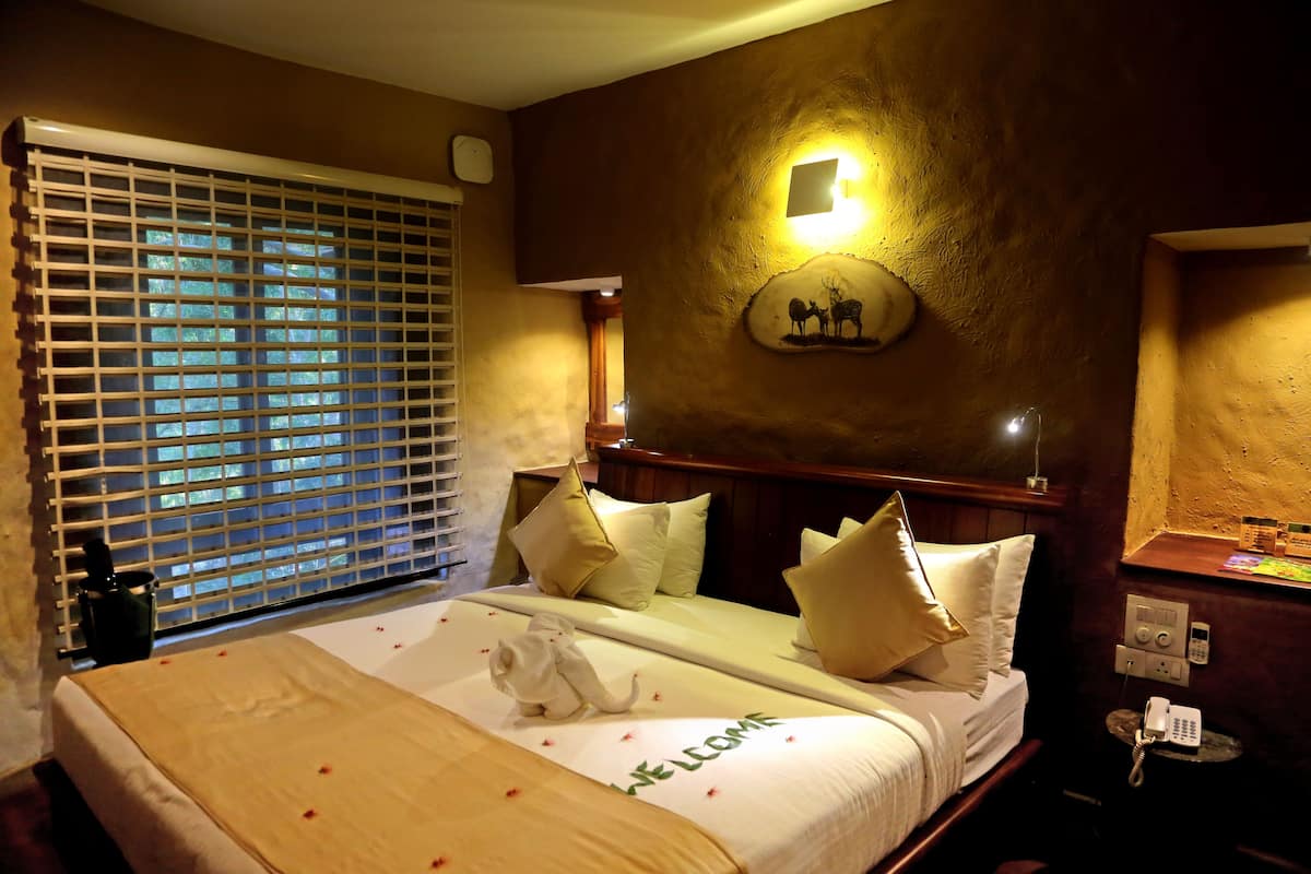 Una habitación de hotel con una cama, una mesita de noche con teléfono, una lámpara en la pared y una ventana con persianas.