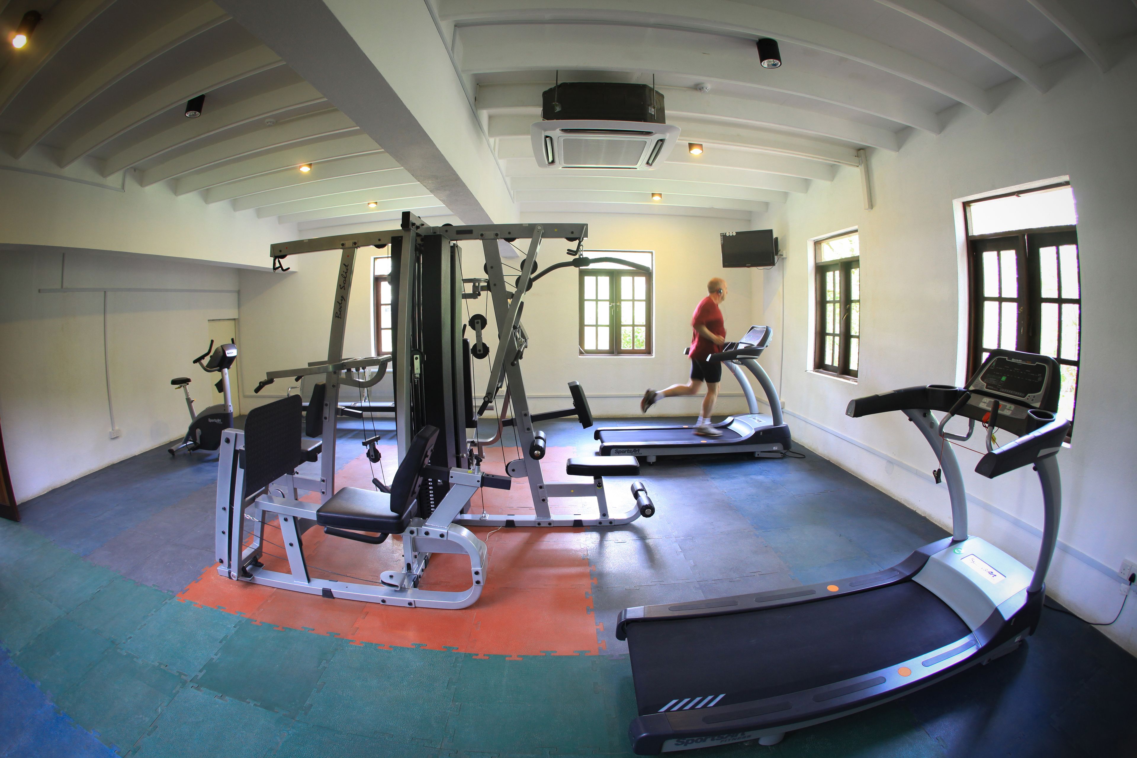 Un gimnasio con cintas de correr, máquinas de pesas y un amplio ventanal que proporciona luz natural.