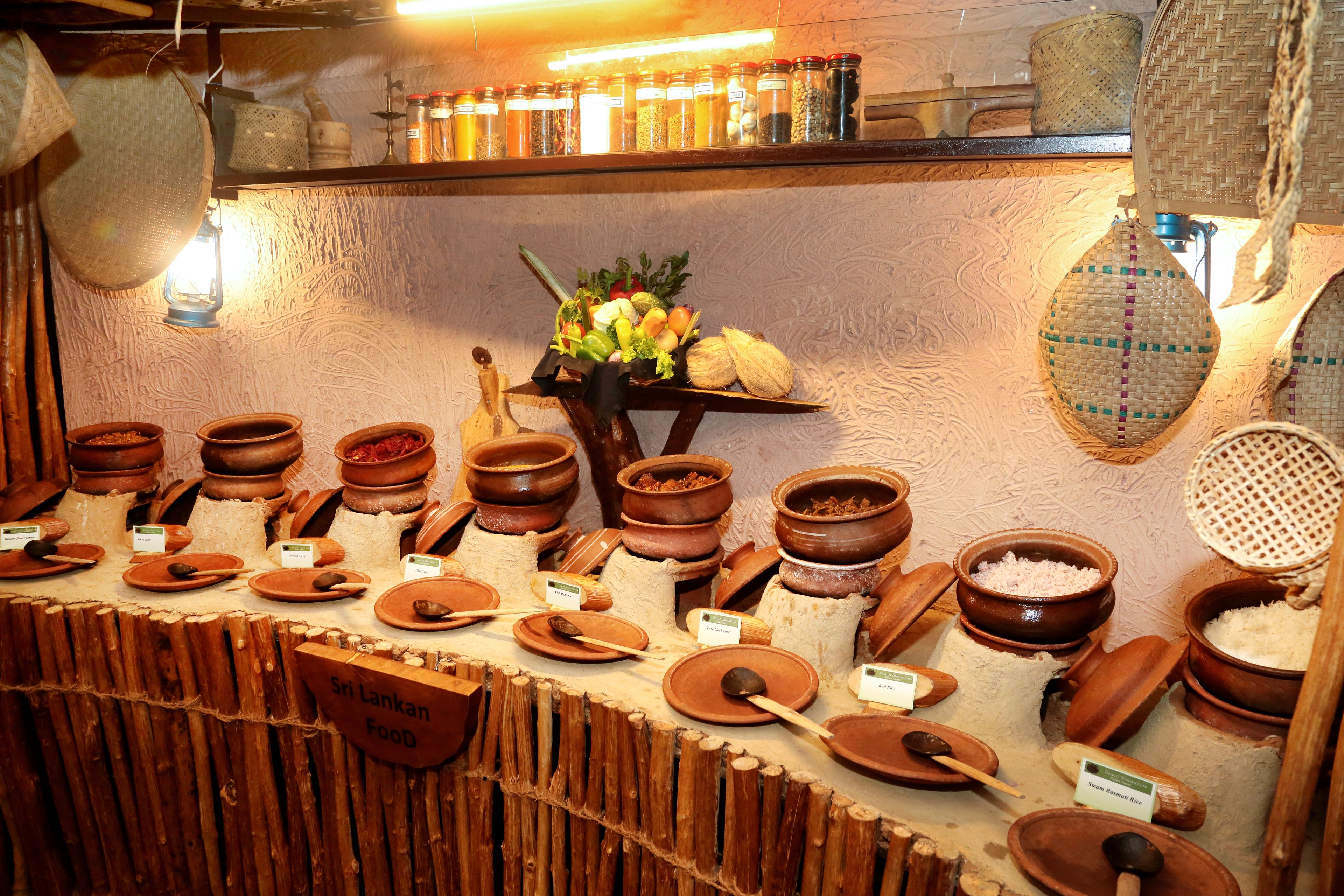 Exposição de comidas tradicionais do Sri Lanka em potes de barro, com etiquetas e uma placa indicando o tipo de alimento.