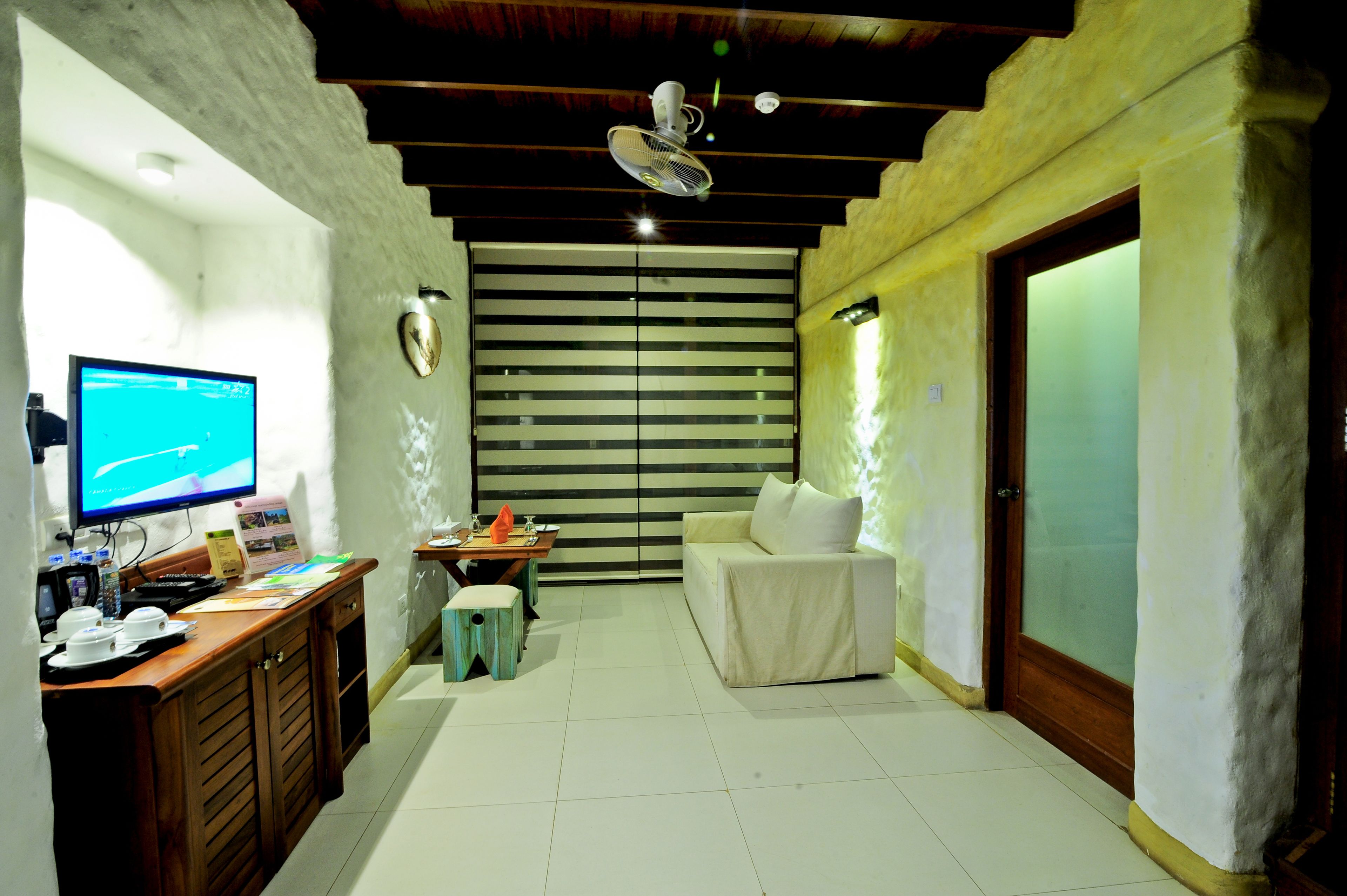 A hotel room with a desk, a sofa, a TV, and a sliding door.