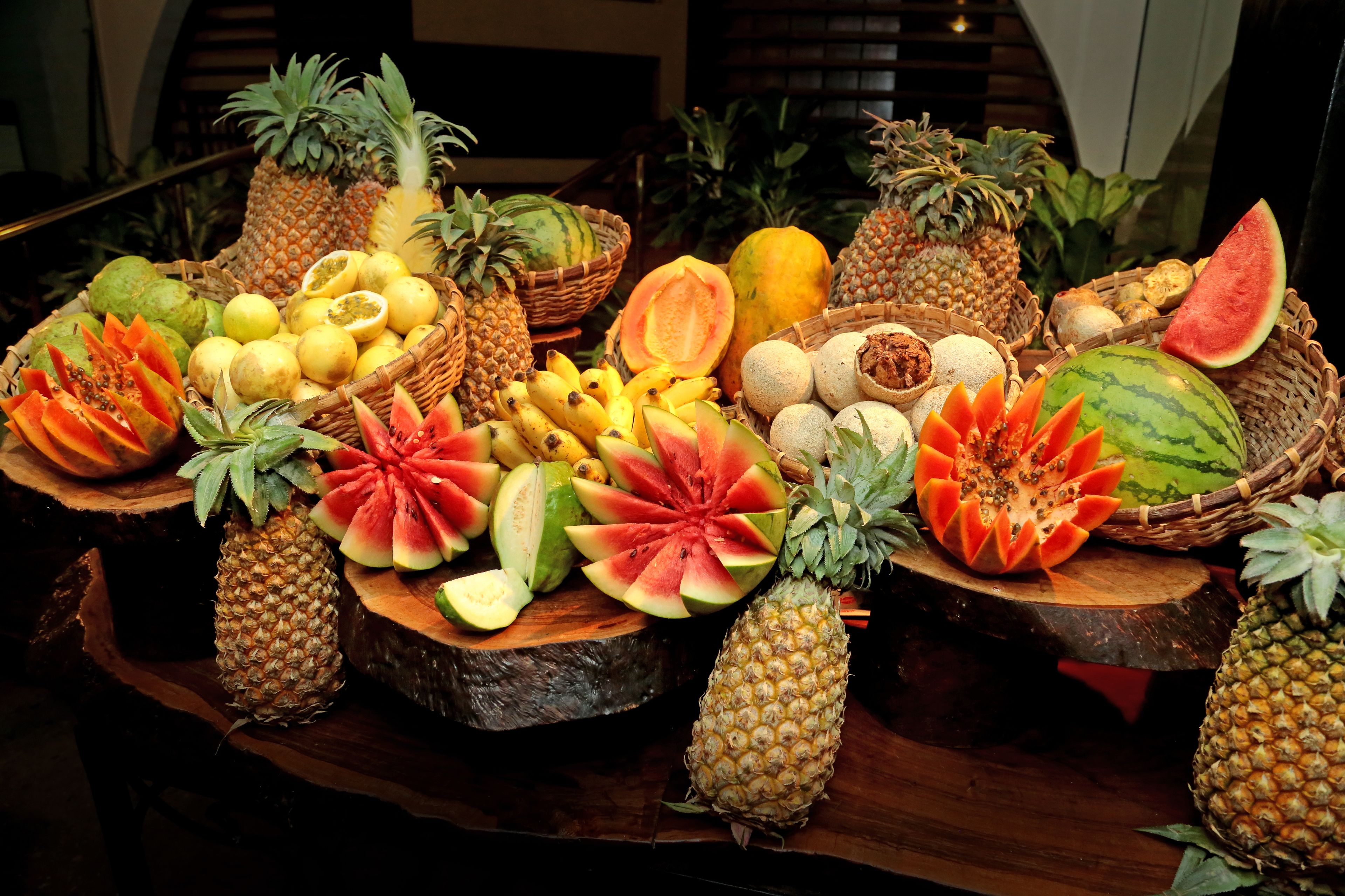 Una varietà di frutta esposta su assi di legno, tra cui ananas, angurie e papaya.