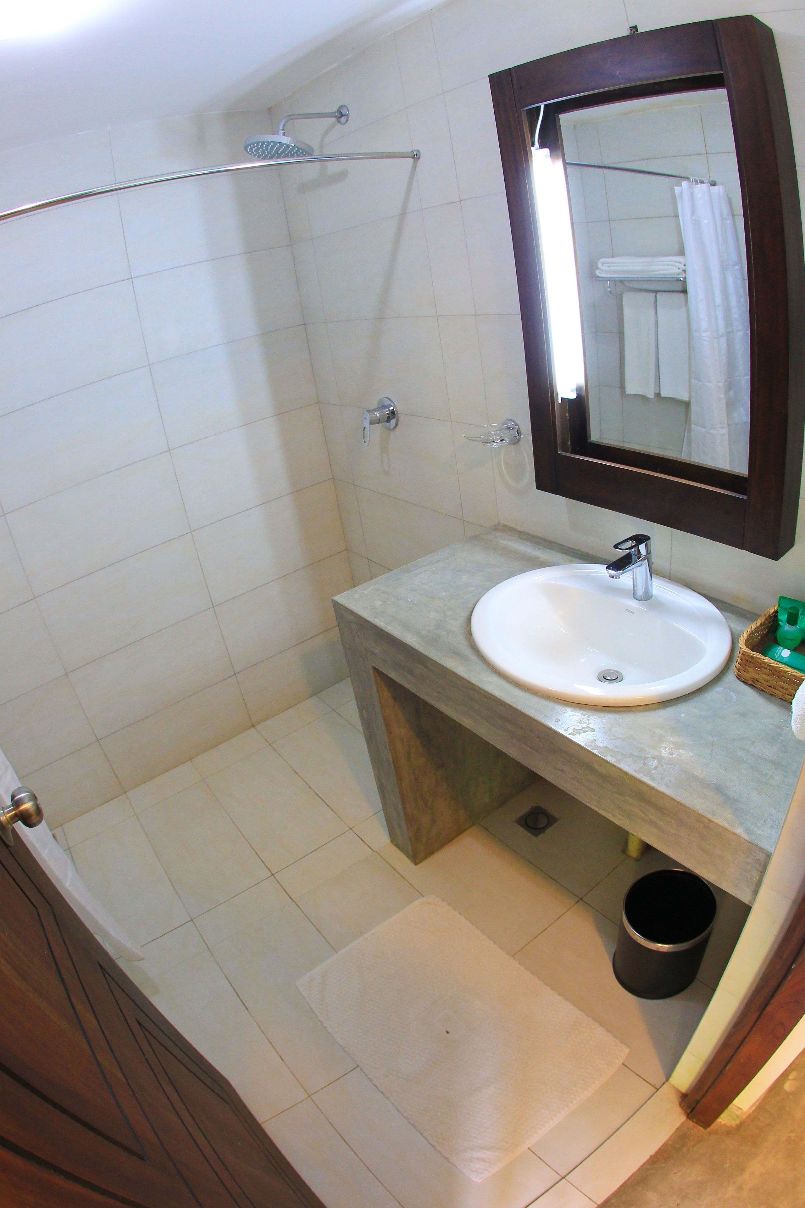 A bathroom with a sink, mirror, shower, and a small trash bin.