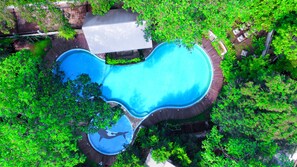 Vista aérea de una piscina de forma peculiar rodeada de abundante vegetación y un edificio pequeño.