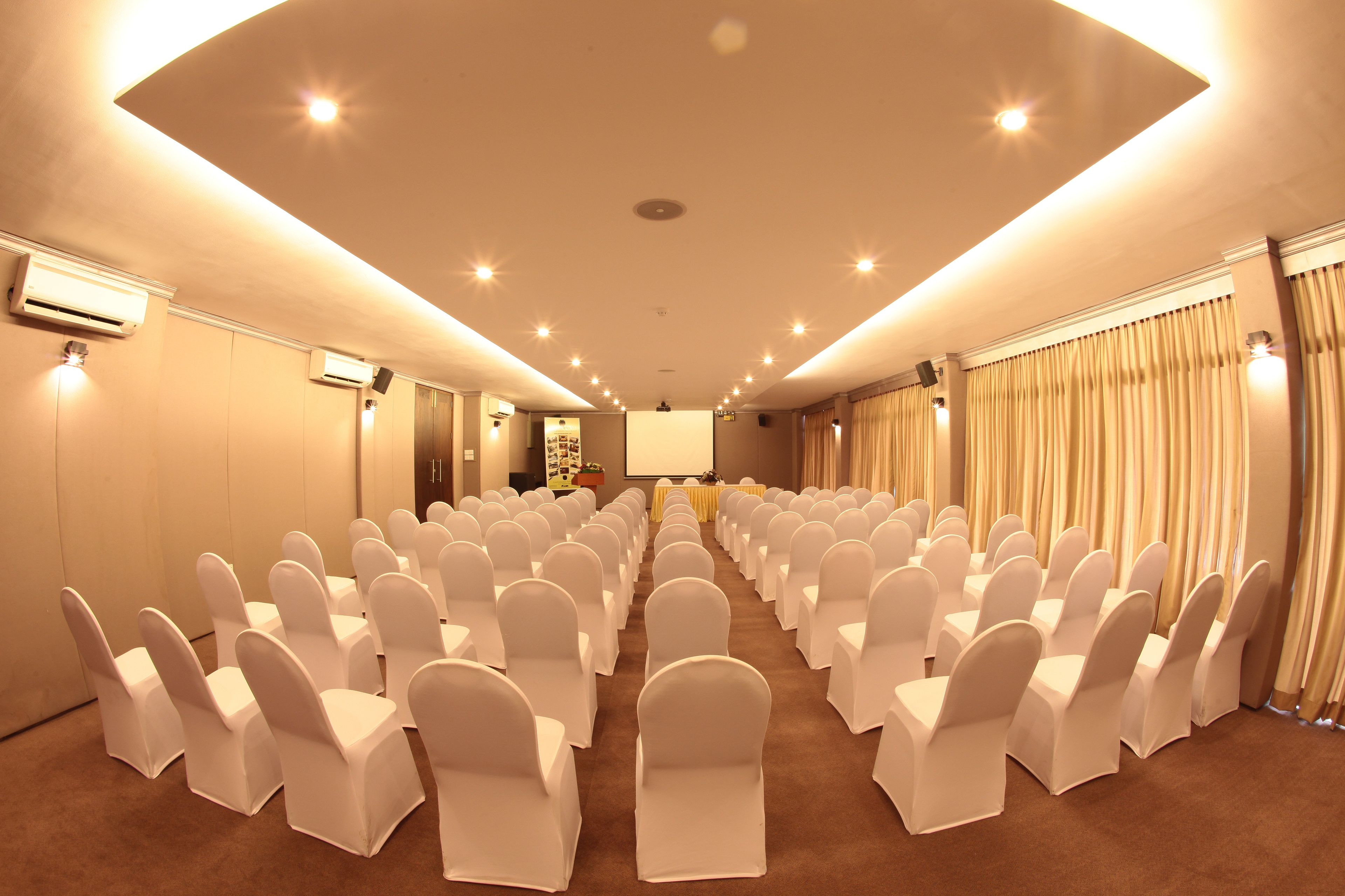 A conference room with rows of white chairs, a projector screen, and a stage.