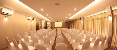 A conference room with rows of white chairs, a projector screen, and a stage.