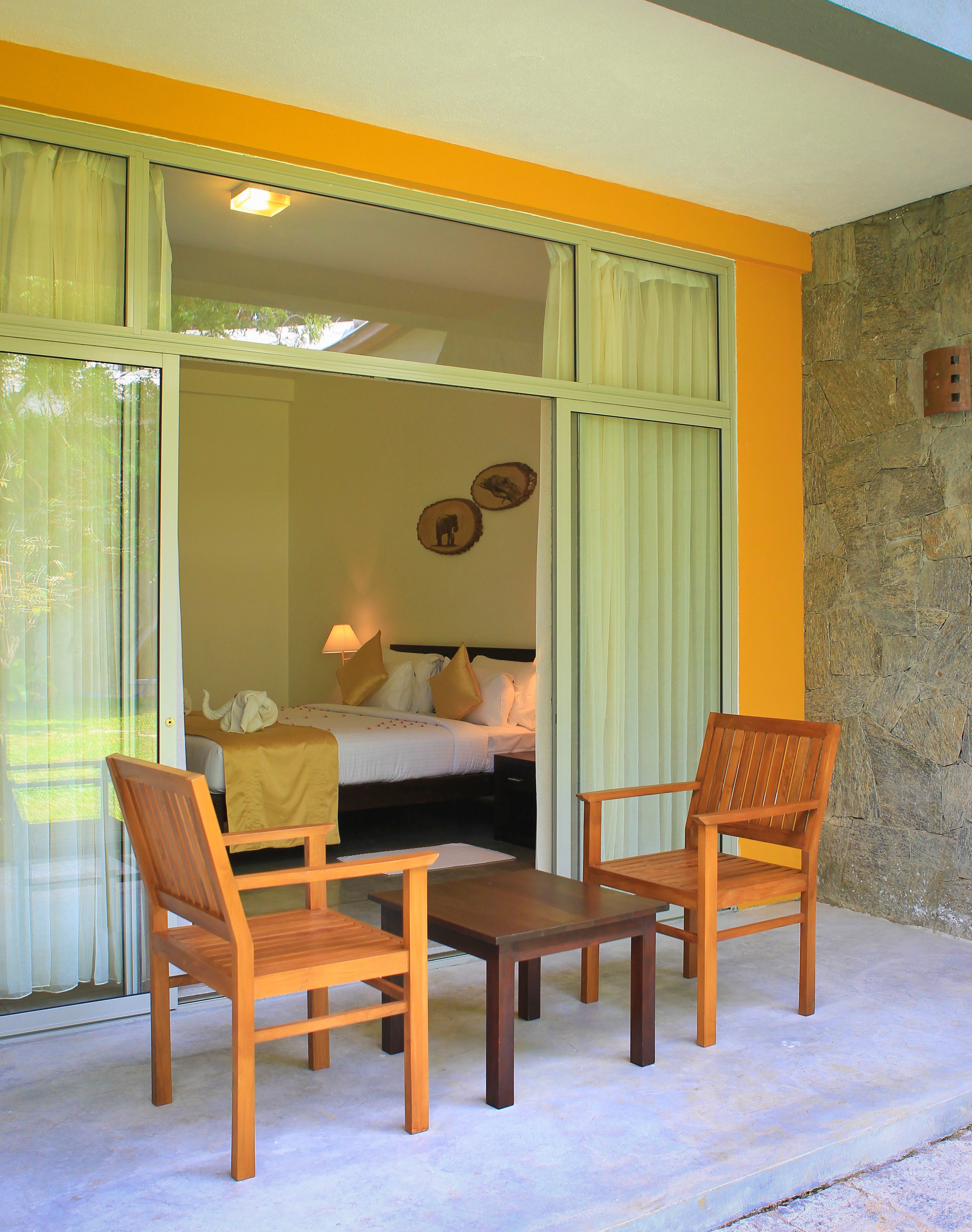 A room with a bed, two wooden chairs, a table, and a view through a glass door.