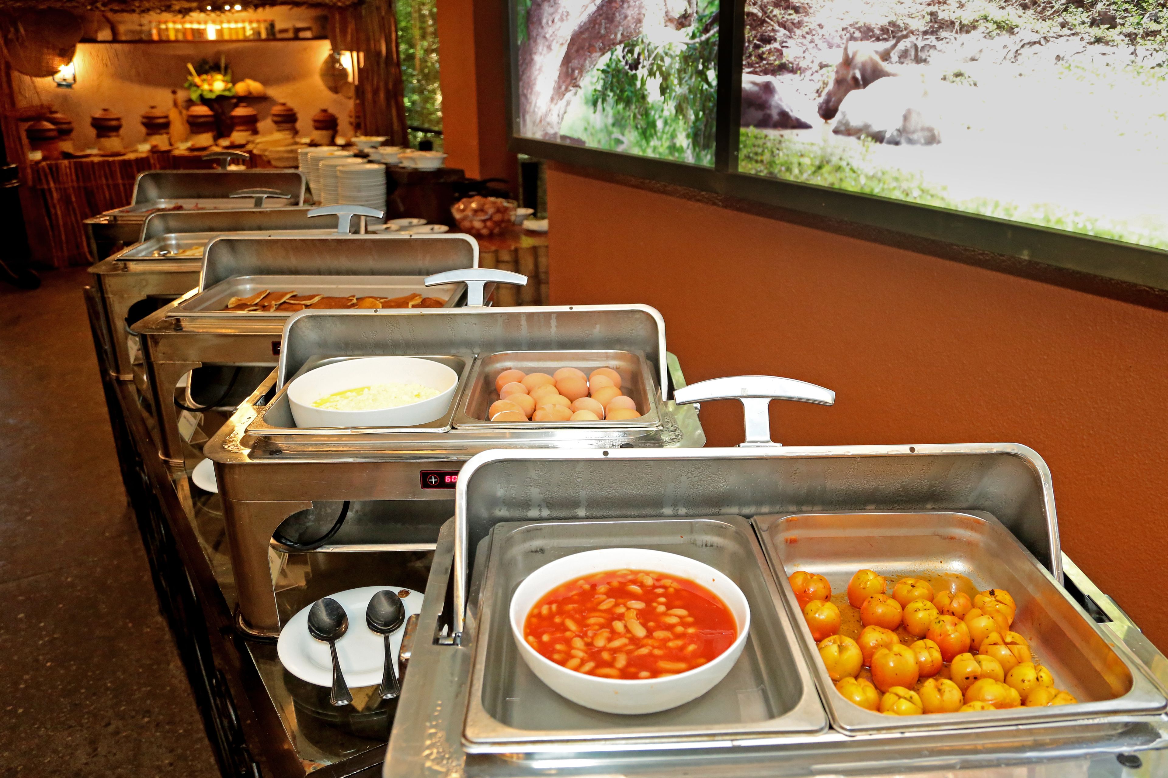 A buffet line with various food options including bowls of soup, eggs, and roasted potatoes.