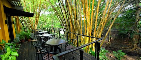 An outdoor dining area with bamboo trees, wooden tables, and chairs.