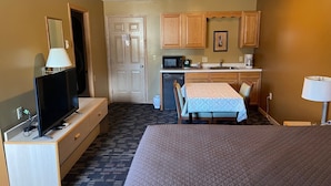 A hotel room with a bed, a TV, a desk, a chair, a small kitchenette, and a door. - Lakeside Motor Inn (Gladstone)