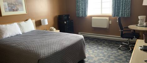Ein Hotelzimmer mit einem großen Bett, einem Schreibtisch, einem Stuhl, einer Mikrowelle, einem Telefon und einem Fenster mit Vorhängen.