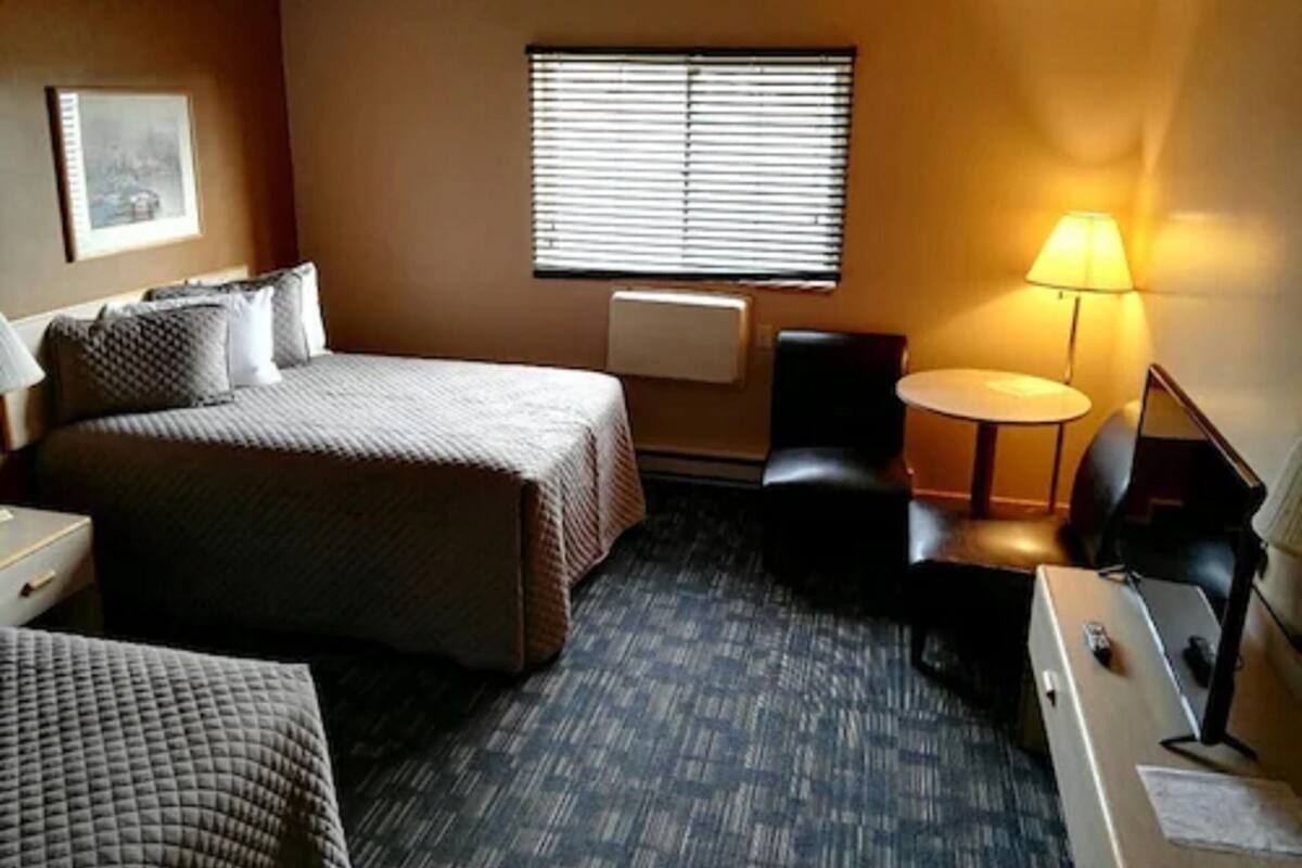 A hotel room with a bed, a desk, a chair, a lamp, and a window with blinds.