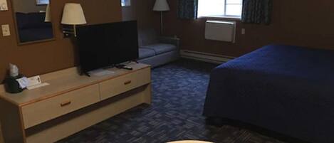 Habitación de hotel con cama, escritorio con televisor, silla, lámpara y ventana con cortinas.