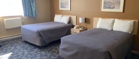 A hotel room with two beds, a nightstand with a lamp, a telephone, and two framed pictures on the wall.