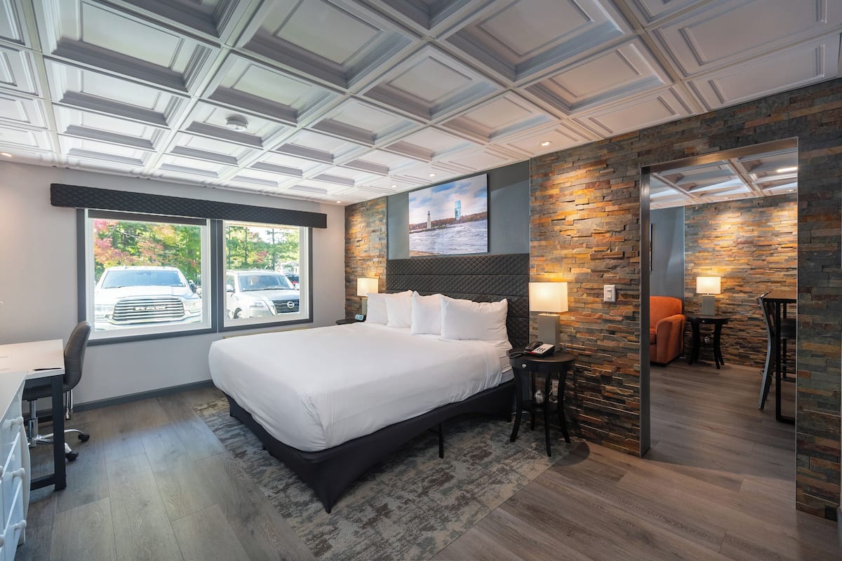 A modern hotel room with a large bed, a desk, and a view of parked cars outside.