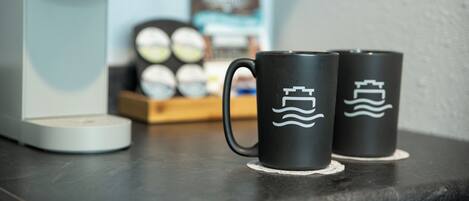Two black mugs with wave designs on a table next to a coffee maker.
