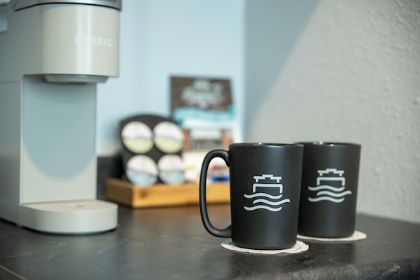 Two black mugs with wave designs on a table next to a coffee maker.