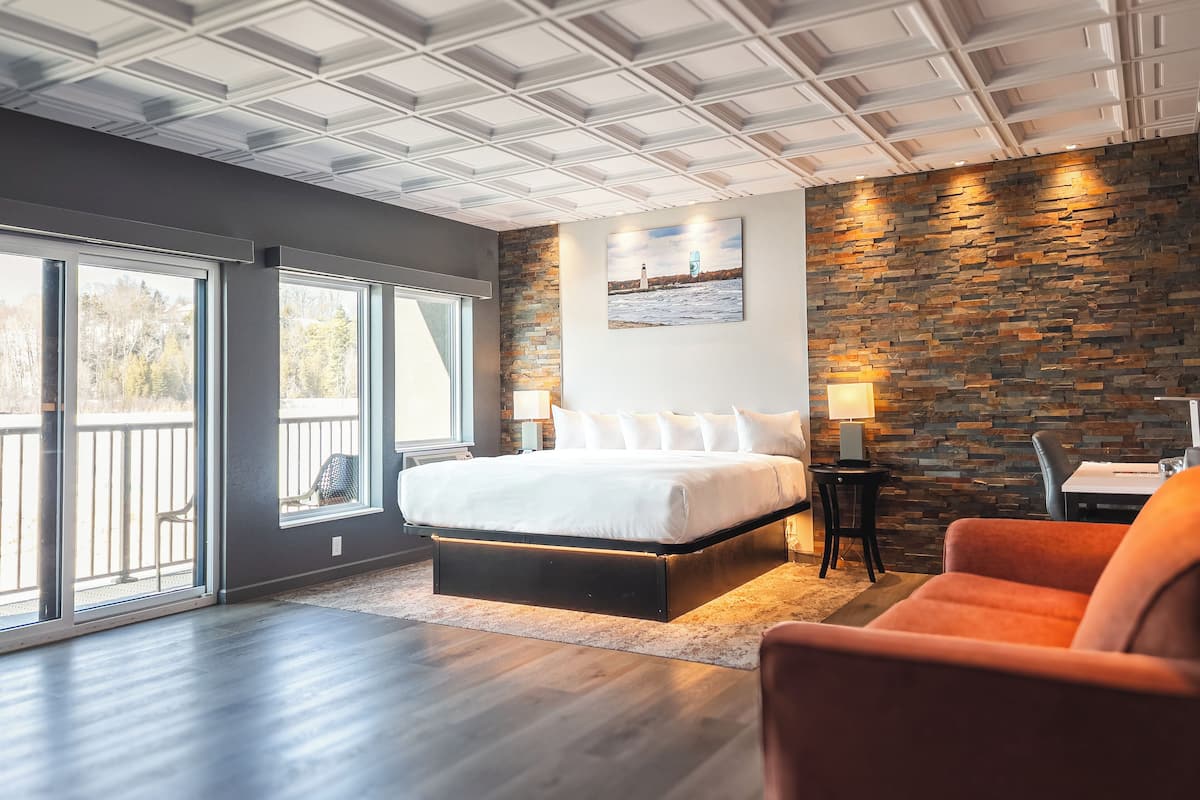 A modern hotel room with a large bed, a stone accent wall, and a balcony with a view.
