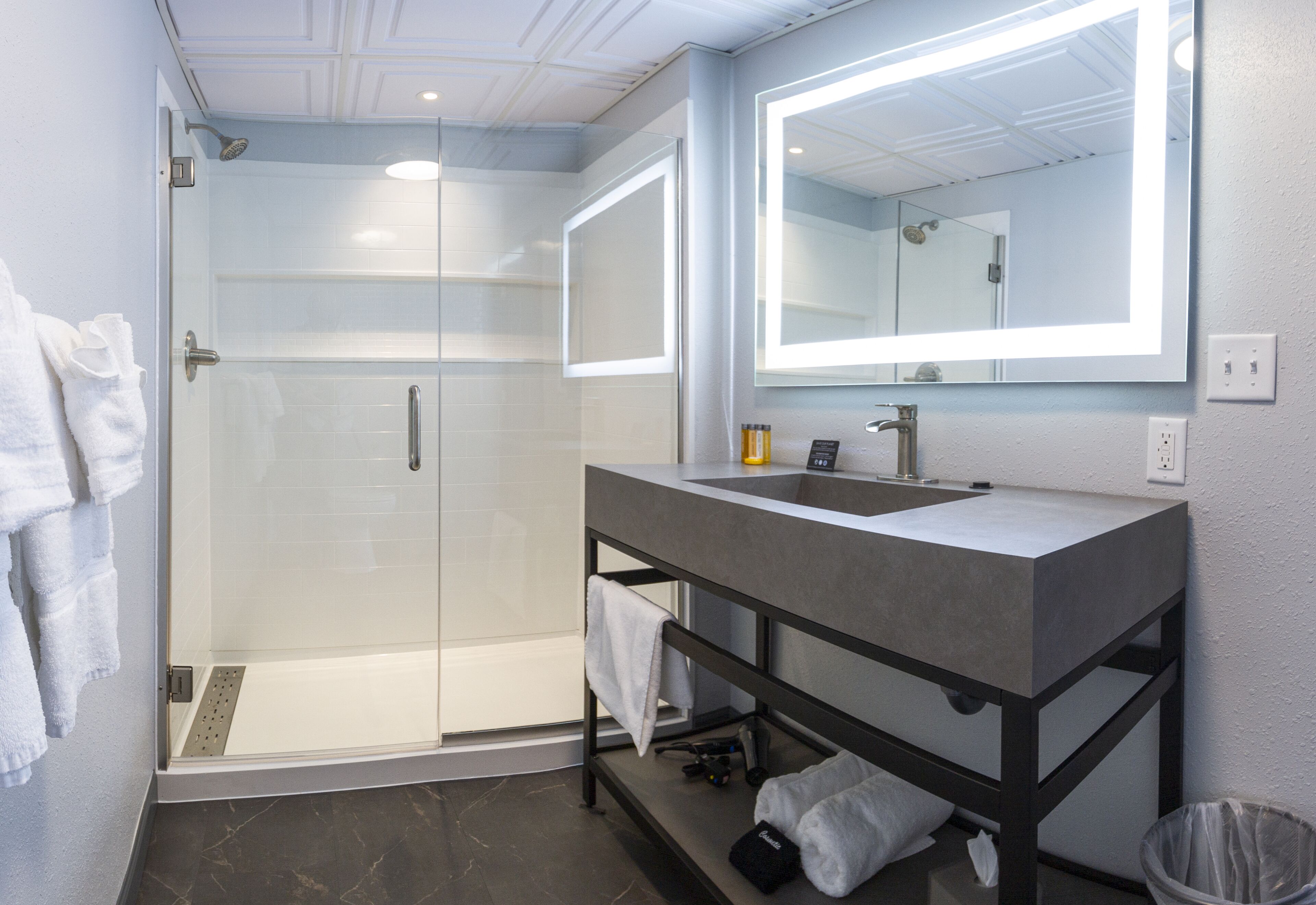 A modern bathroom with a glass-enclosed shower, a vanity with a large mirror, and a towel rack.