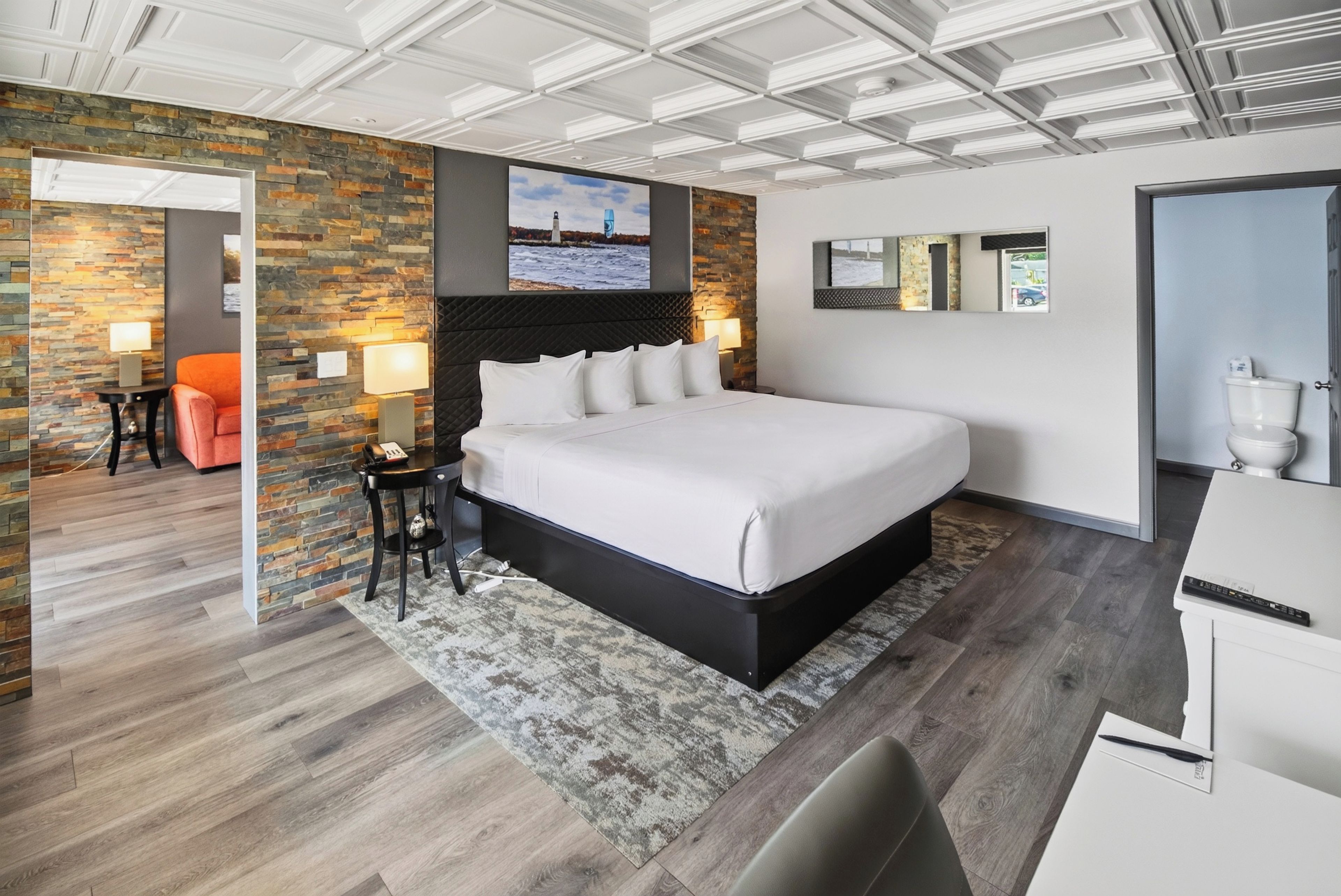 A modern bedroom with a large bed, a stone accent wall, and a ceiling with recessed lighting.