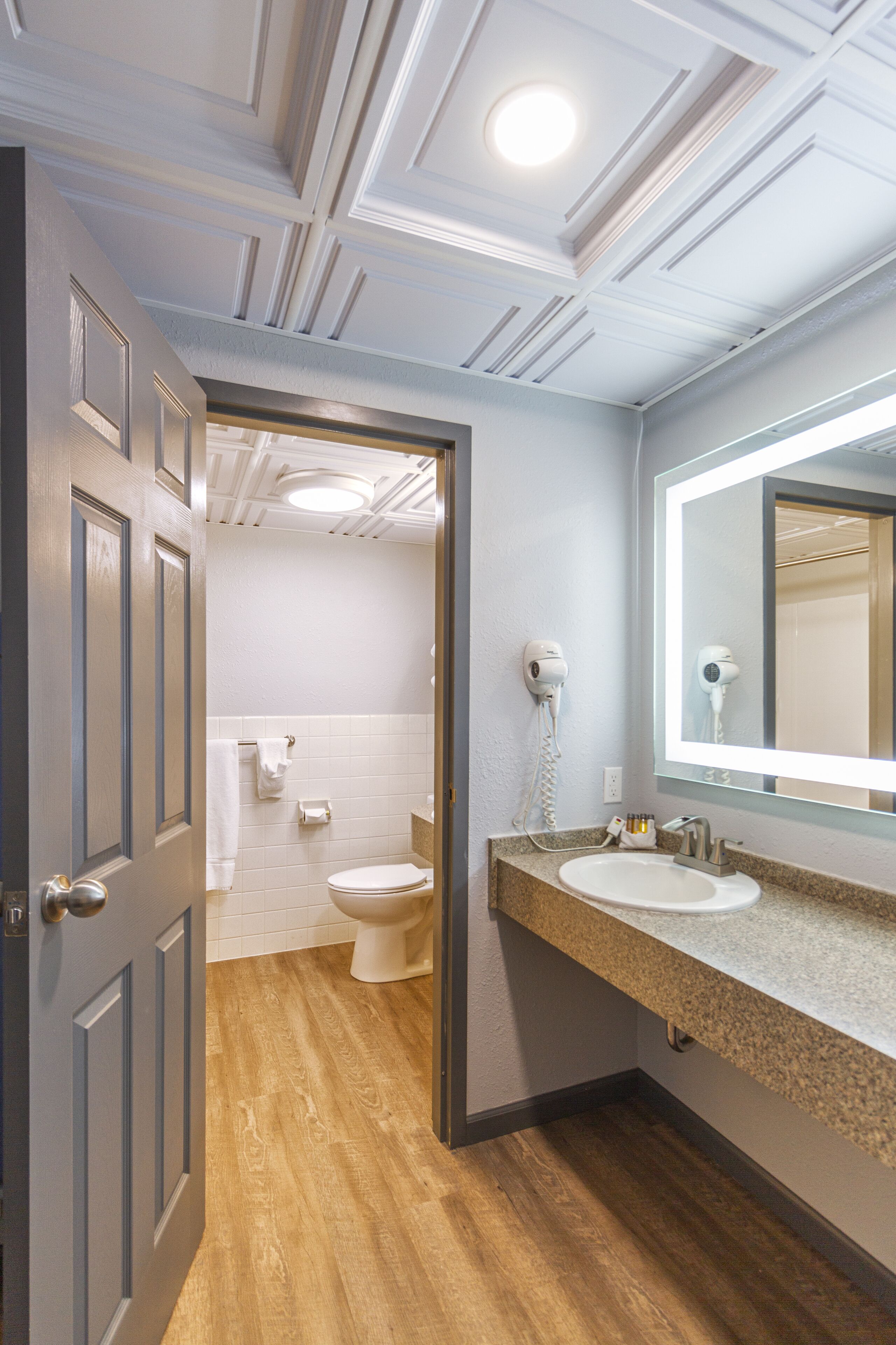 A bathroom with a wooden floor, a white sink, a mirror, and a hairdryer on the wall.