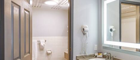 A bathroom with a wooden floor, a white sink, a mirror, and a hairdryer on the wall.