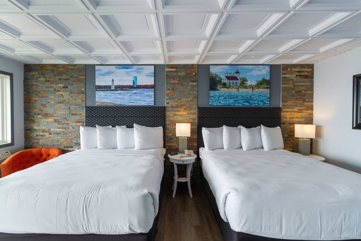 A hotel room with two beds, a brick accent wall, and a view of a lighthouse and beach.