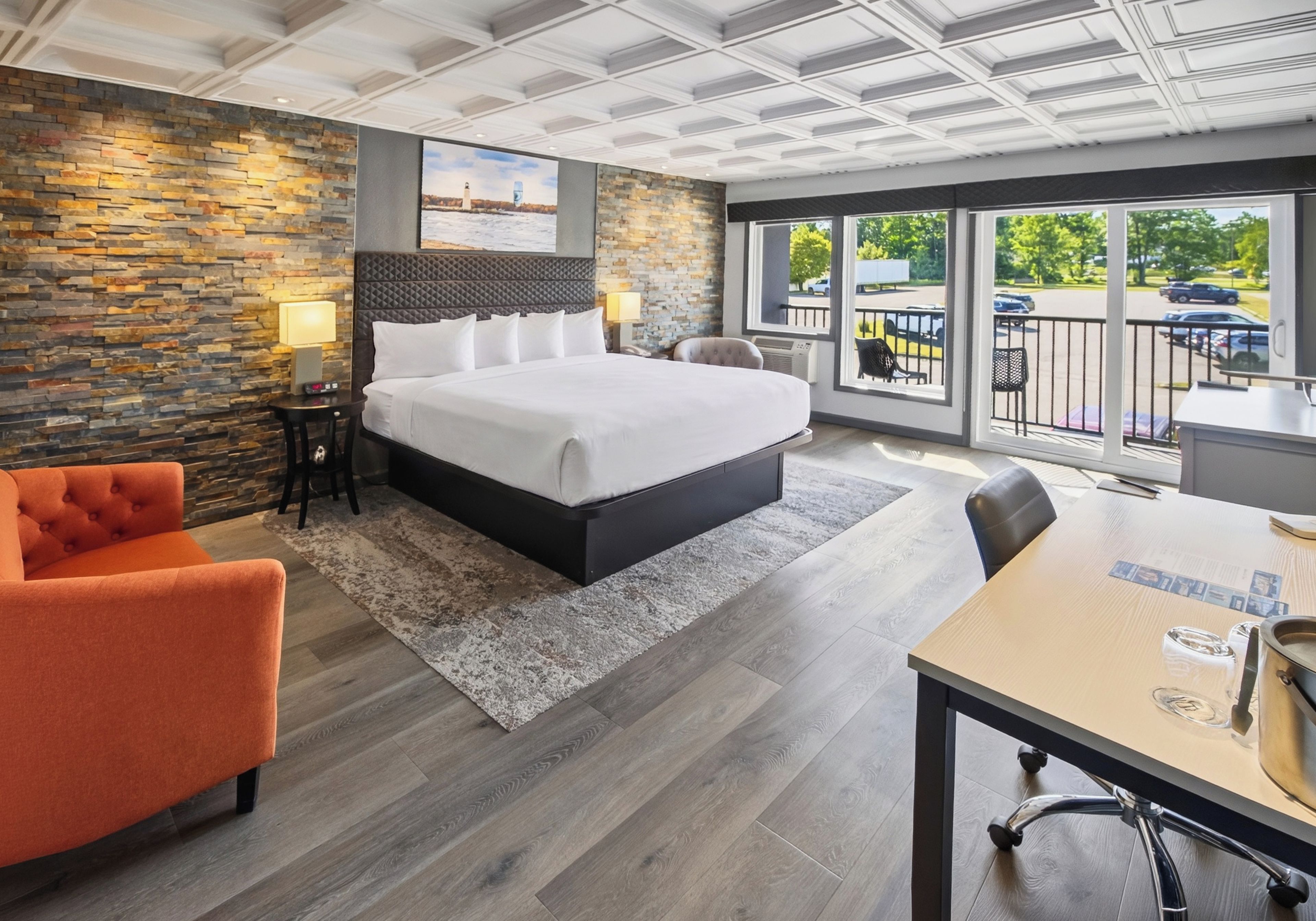 Ein Hotelzimmer mit einem großen Bett, einer Wand mit Steinverkleidung, Blick durch einen Balkon und einem Essbereich.