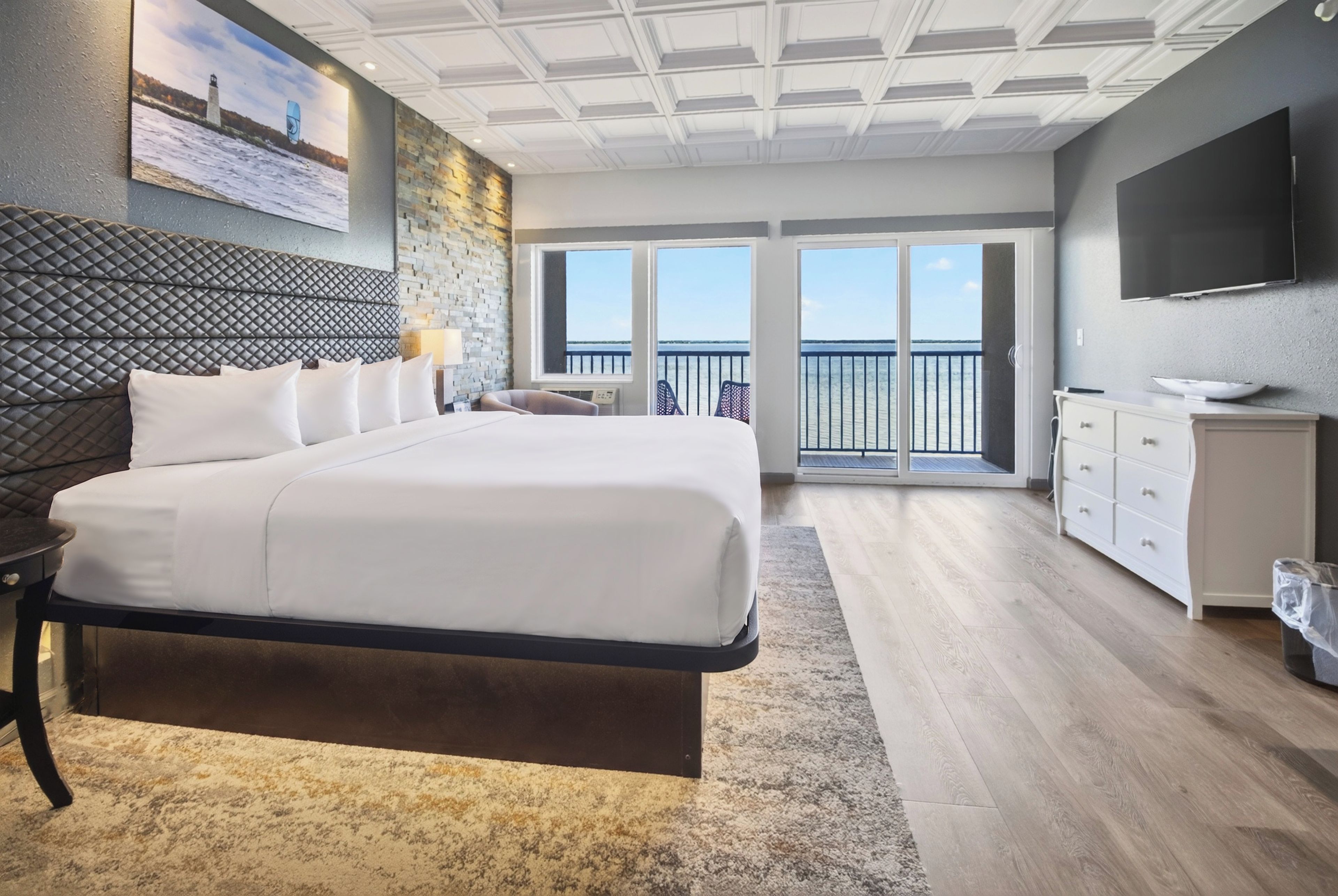 A hotel room with a large bed, a TV, a balcony with a view, and a stone wall.