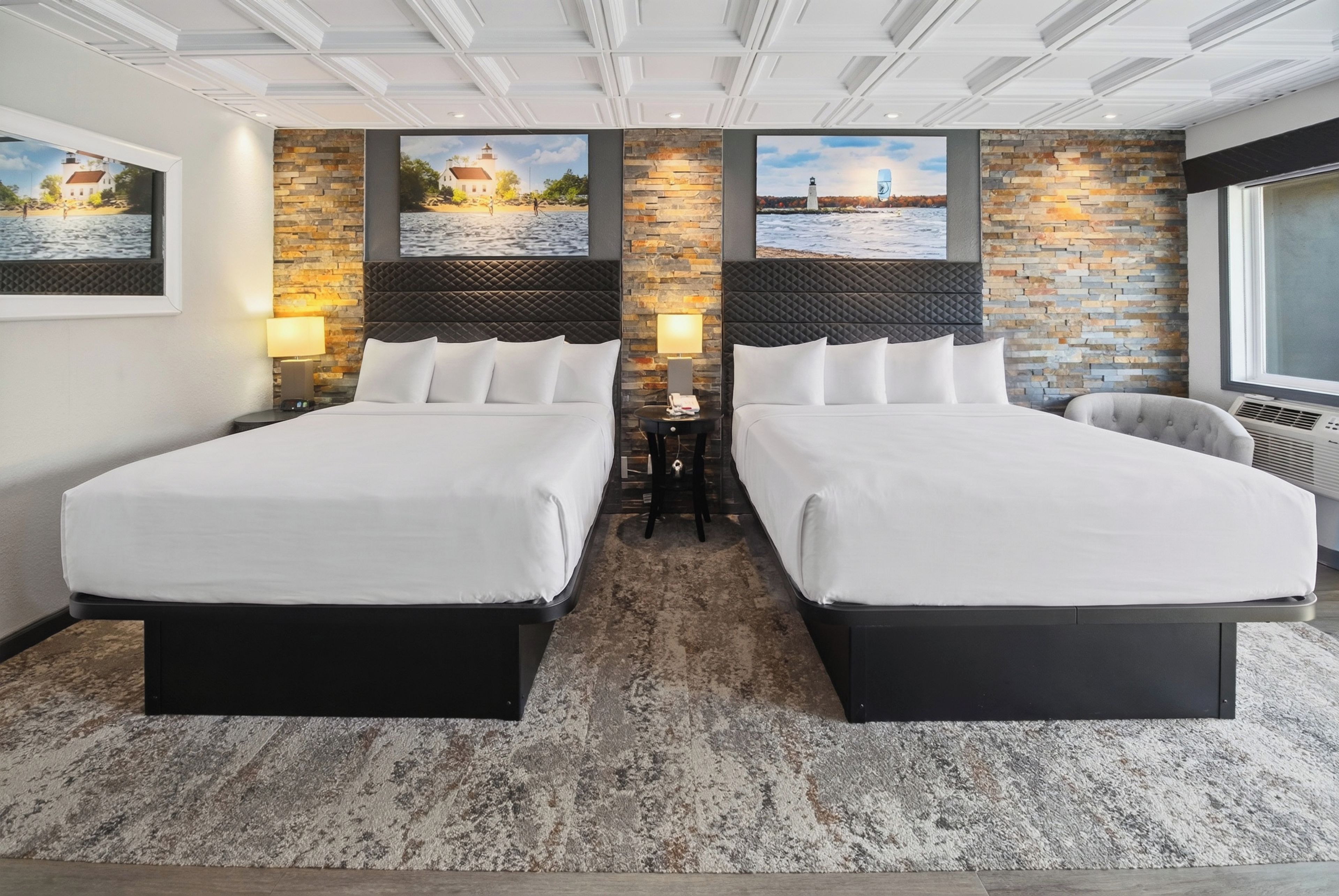A hotel room with two beds, a stone accent wall, and artwork depicting coastal scenes.