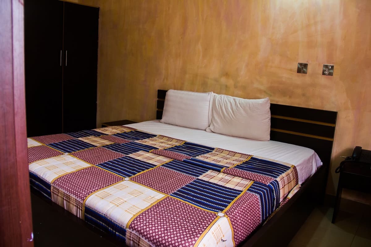 A hotel room with a large bed, a wooden wardrobe, and a nightstand with a phone.