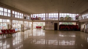 Un vaste hall doté de hauts plafonds et de grandes fenêtres, avec des rangées de chaises et de tables rouges, ainsi qu’un espace balcon.