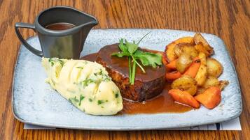 A plate of food with a meat patty, mashed potatoes, and roasted vegetables, accompanied by a gravy cup.