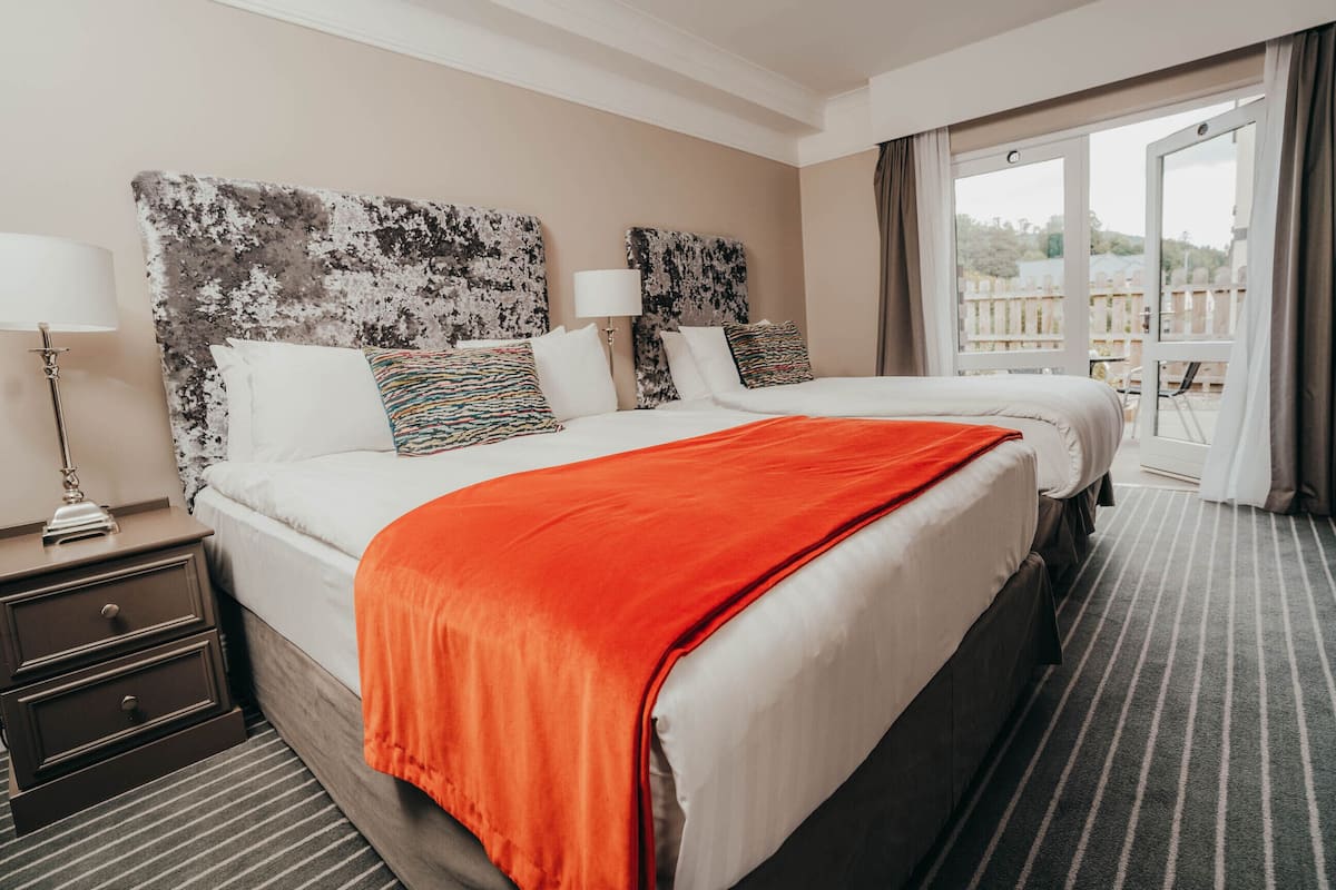 Ein Hotelzimmer mit einem großen Bett, zwei Nachttischen und Blick ins Freie durch ein Fenster.