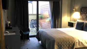 A hotel room with a bed, a desk, a chair, a TV, and a balcony with a view of the outside.