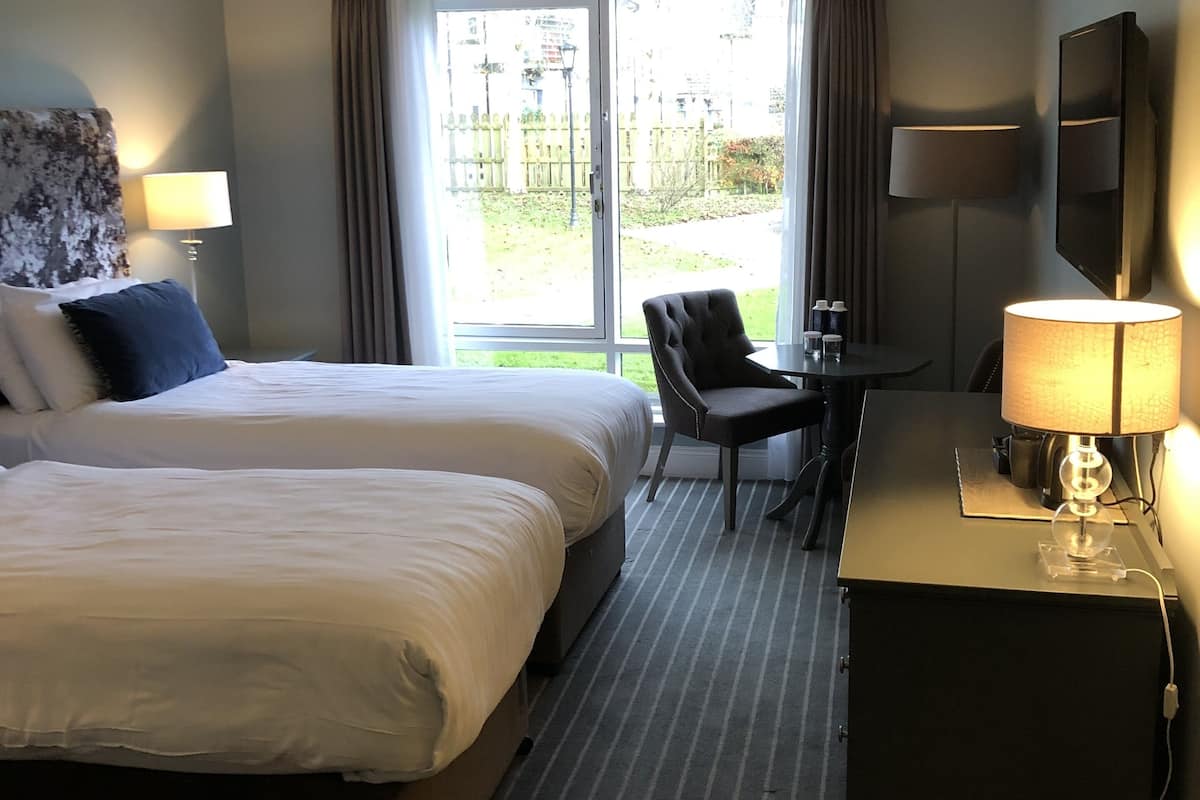 Ein Hotelzimmer mit zwei Betten, einem Schreibtisch mit Lampe, einem Sessel und einem Fernseher.