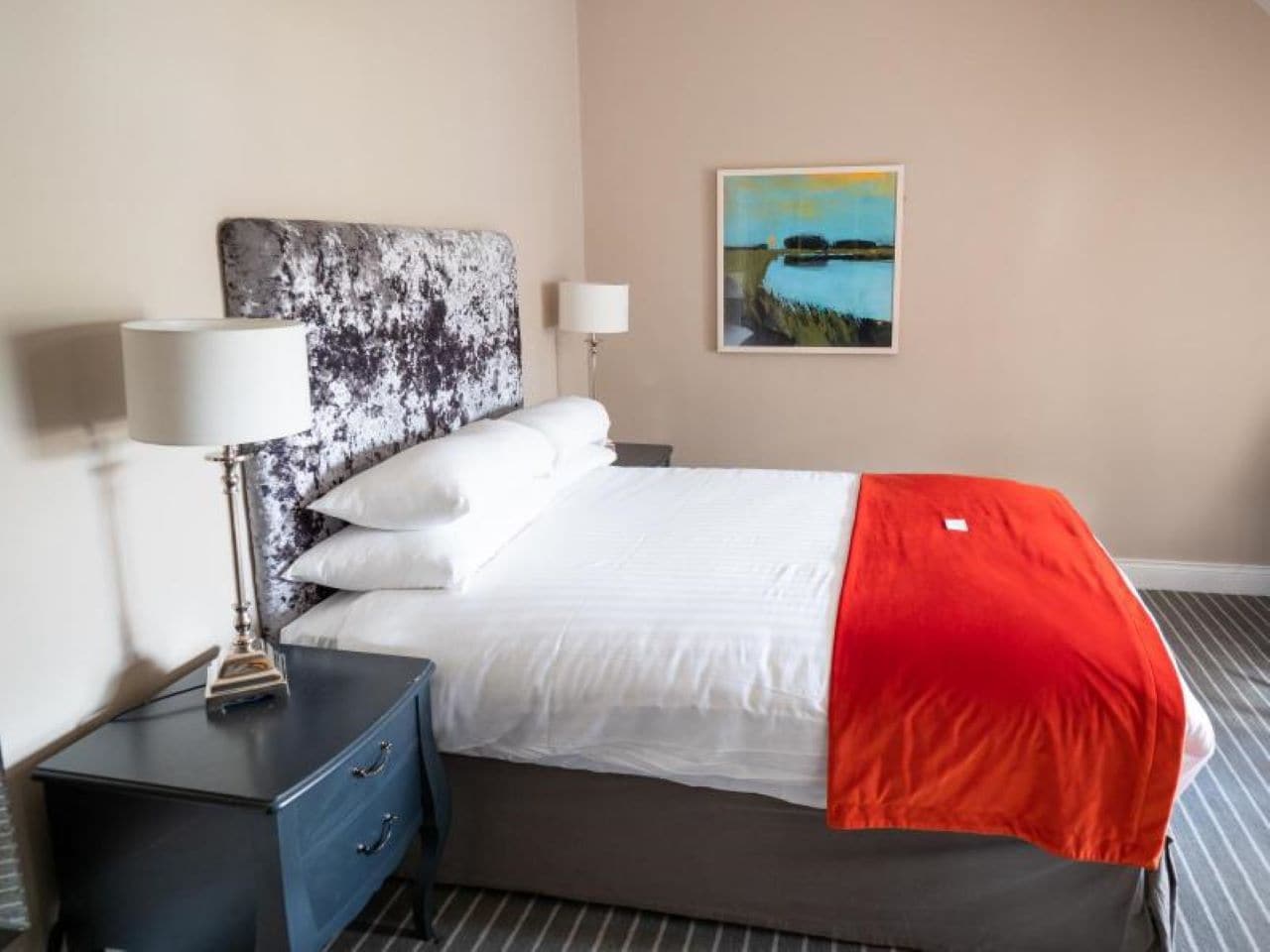 Una habitación de hotel con una cama, una mesita de noche, una lámpara y un cuadro en la pared.