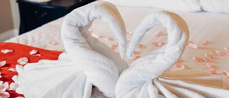 A bed with two white towels shaped like swans, a red bedspread, and two small gift boxes on the bed.