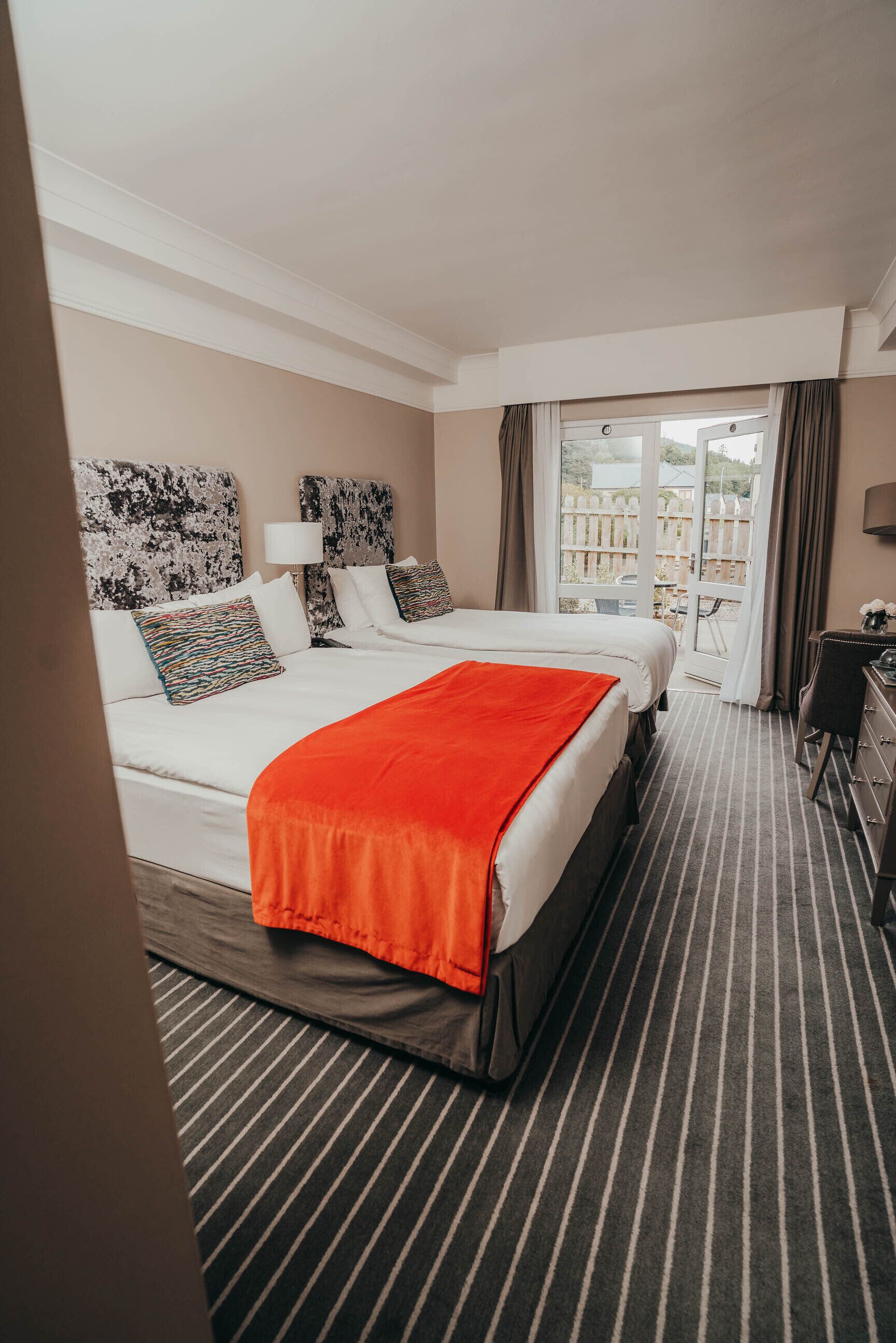 A hotel room with two beds, a desk, and a view of the outdoors.