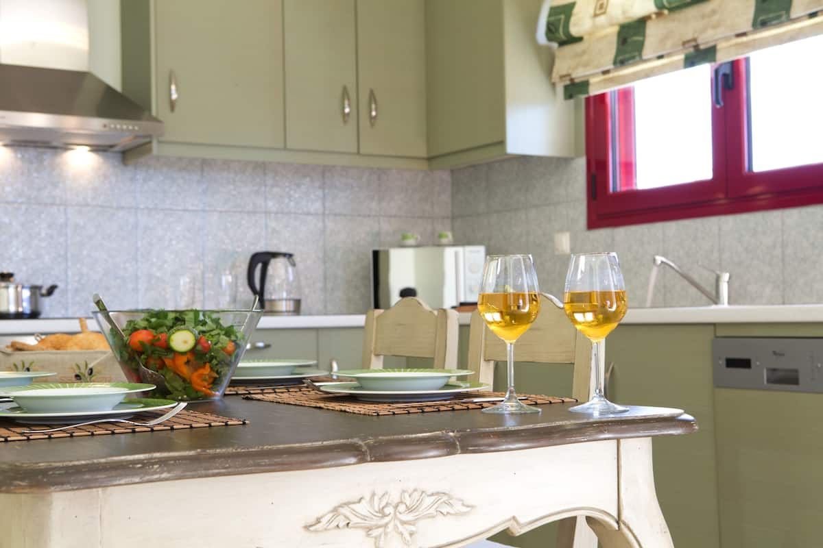 A kitchen with a dining table set for two, a glass of white wine, and a salad bowl.