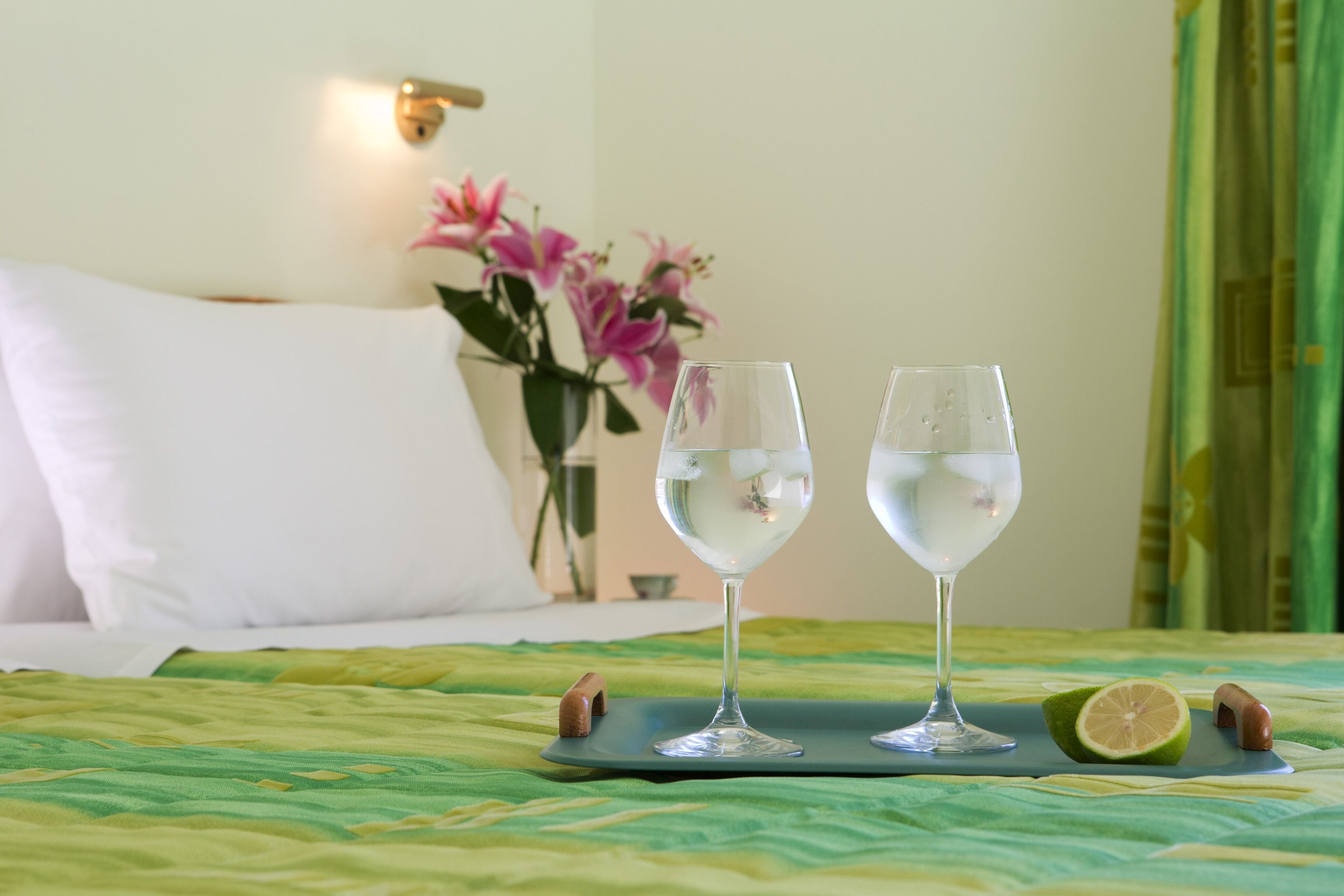 A bed with a green bedspread, two glasses of water, and a half-cut lime on a tray.