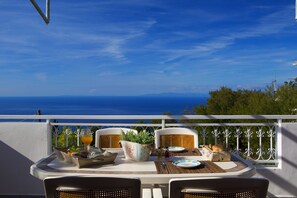 A table set for two with a view of the sea, a potted plant, and a basket of bread on a balcony. - Exanthia Villas (Lefkada)