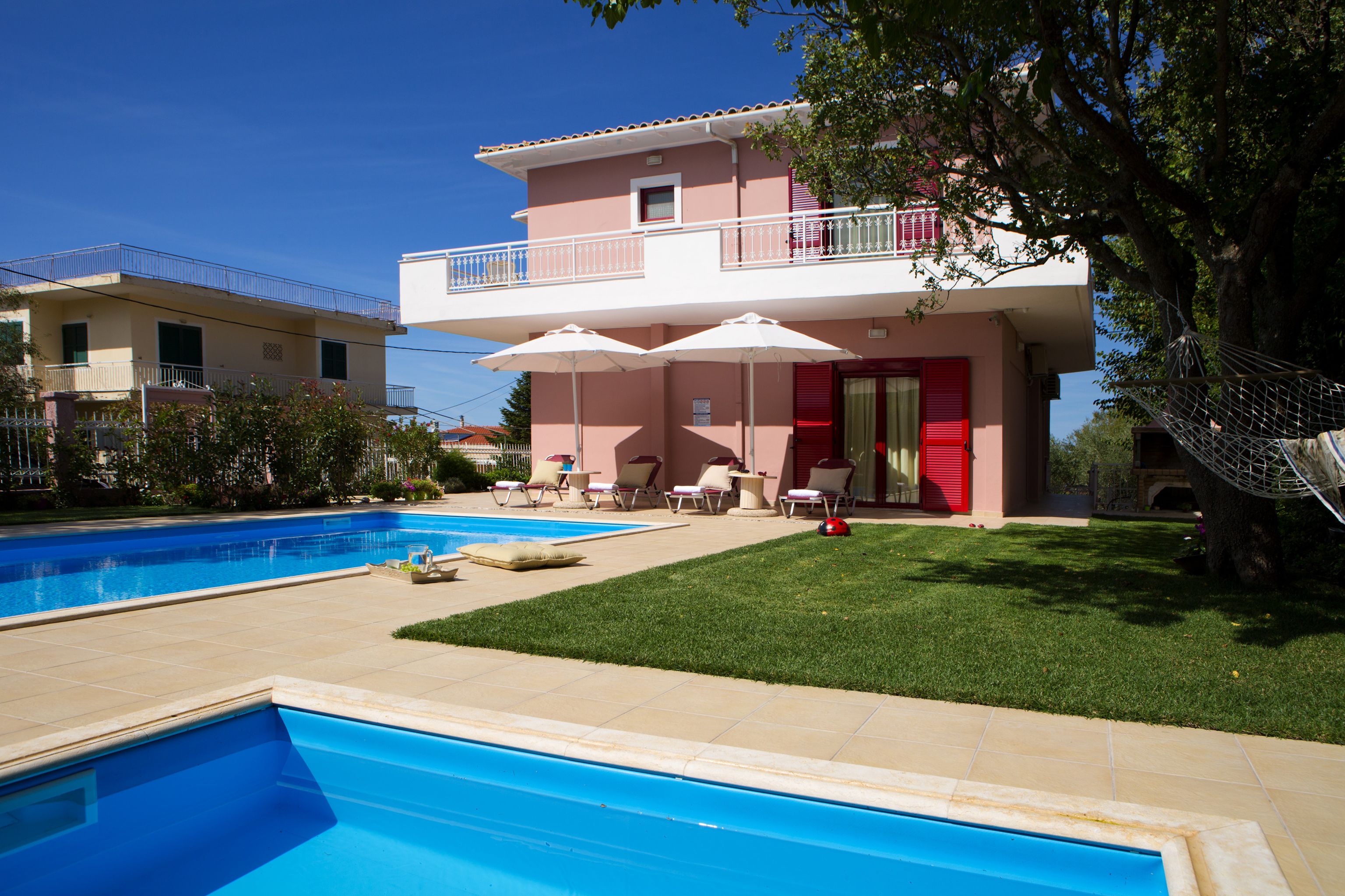 Un edificio de dos pisos con piscina, asientos exteriores y una hamaca.