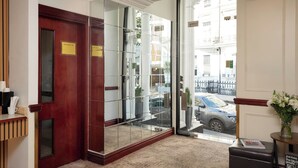 A hotel lobby with a reception desk, a glass door entrance, and a view of the street outside. - The Prime London Hotel (London)