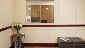 A reception area with a check-out counter, a small table with a vase of flowers, and a leather bench with a magazine. - The Prime London Hotel (London)