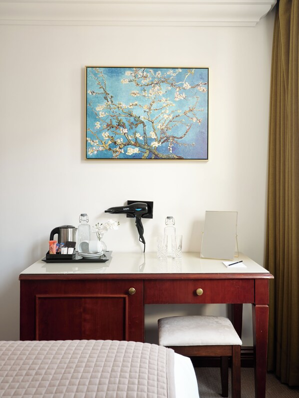 A hotel room with a wooden desk, a bed, and a painting of a tree with blossoms. - The Prime London Hotel (London)