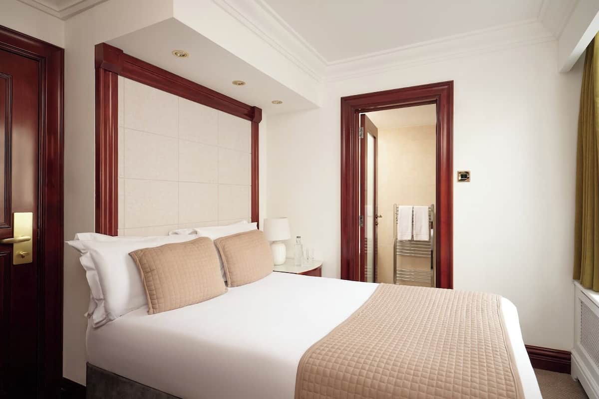 Camera d'albergo con un letto grande, un comodino, uno specchio e una porta che dà su un bagno.