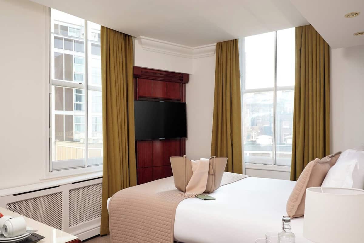 Una camera d'albergo con un letto grande, una TV a muro e una finestra con tende.
