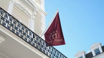 A building with a balcony featuring ornate black metal railings and a maroon flag with "THE PRIME HOTEL" text.