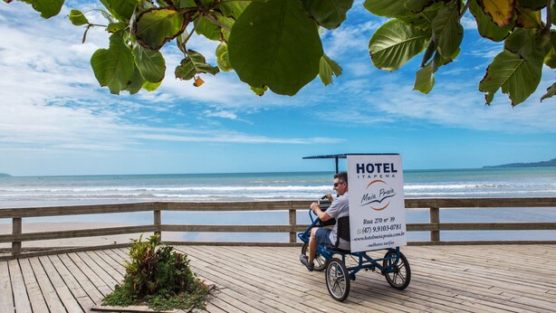Un hombre en silla de ruedas en una pasarela de madera con un letrero que dice HOTEL MEIA PRAIA.